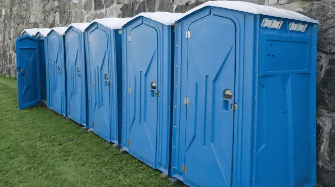 Row of blue portable toilets lined up on grass against a stone wall for event sanitation in Charleston, SC