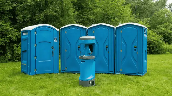 Four blue portable toilets and a matching hand washing station on grass near trees, a common sight at local outdoor events in Charleston, SC