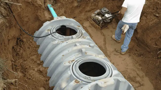 Septic tank installation showing a technician compacting soil around a new poly septic tank in an excavation pit in Charleston, SC